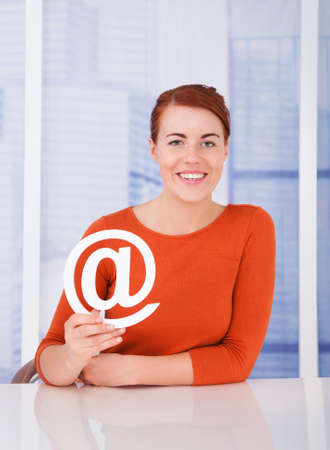 Portrait of beautiful young woman holding internet symbol at deskの写真素材