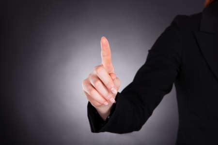 Midsection of young businesswoman touching transparent screen against black 