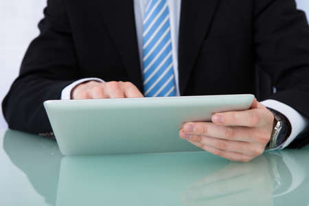 Midsection of young businessman using tablet computer at office desk