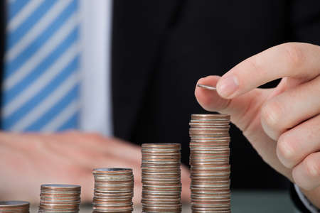 Midsection of young businessman with coins stacked as bar graph at office tableの写真素材