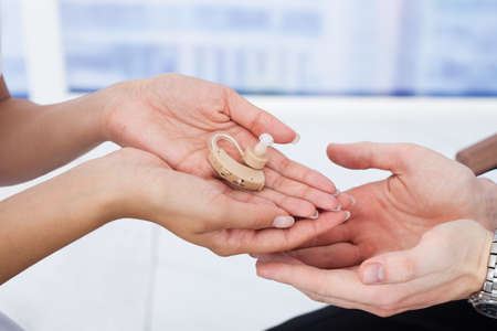 Cropped image of female doctor giving hearing aid to male patient in clinicの写真素材