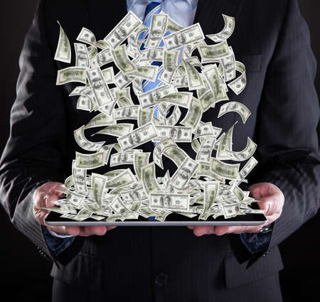 Midsection of businessman holding digital tablet with American banknotes over black 