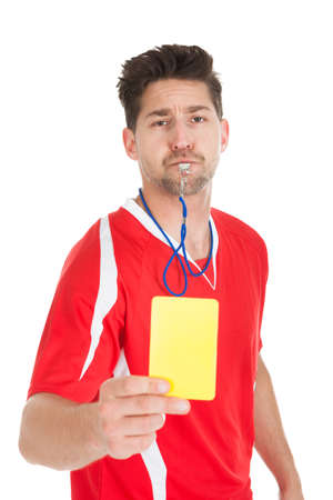 Portrait of referee blowing whistle while showing yellow card over white の写真素材