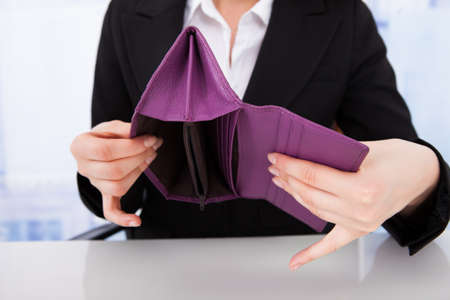 Midsection of businesswoman holding purple empty wallet at office deskの写真素材