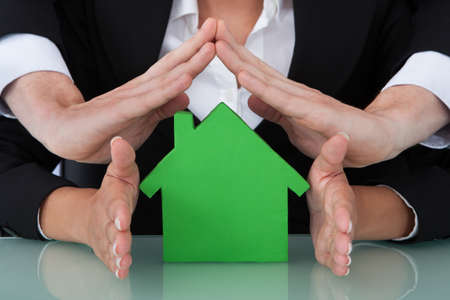 Cropped image of business people sheltering green house model in officeの写真素材