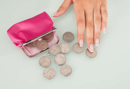 Midsection of businesswoman counting coins spilled from pink purse at office desk