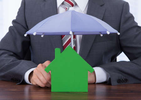 Midsection of businessman sheltering house with umbrella at deskの写真素材