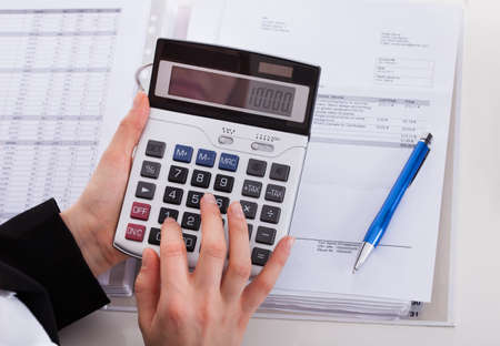 Cropped image of businesswoman using calculator while working at office desk