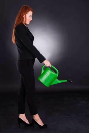 Full length side view of young businesswoman using green watering can against black の写真素材