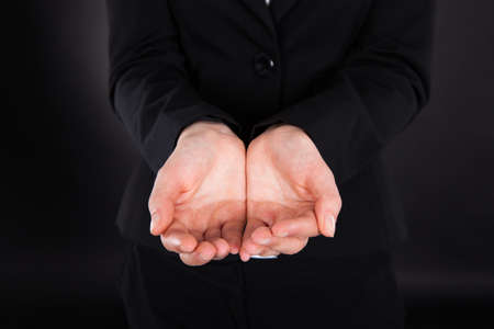 Midsection of young businesswoman with cupped hands standing against black 