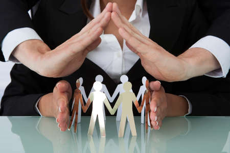 Cropped image of young business people sheltering team of paper people at office deskの写真素材