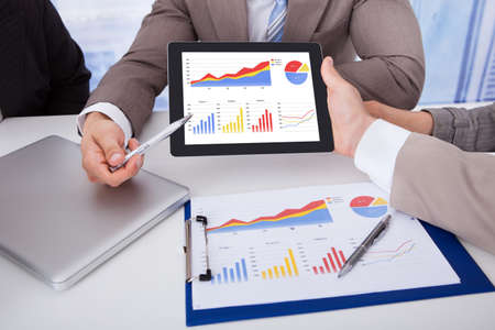 Cropped image of business people discussing graph on digital tablet at table in office