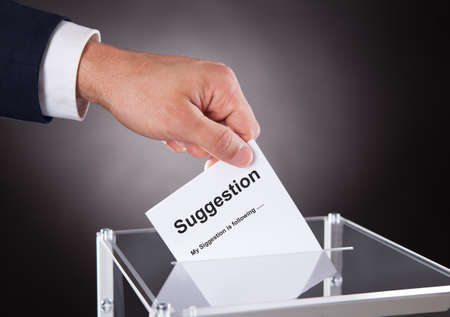Cropped image of businessman placing suggestion slip into box over black background
