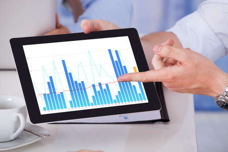 Cropped image of businessman showing graph on digital tablet to colleagues in office