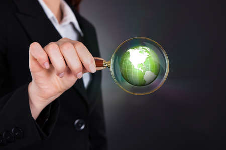 Midsection of businesswoman holding magnifying glass over globe against black background