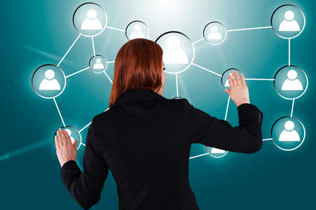 Rear view of businesswoman touching connected human icons over green backgroundの写真素材