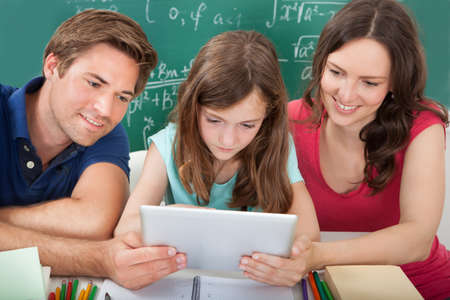 Smiling parents assisting daughter in using digital tablet while studying at home