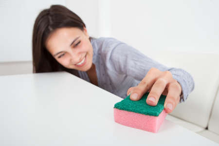 Happy young woman cleaning table with cleanser and rag in houseの写真素材
