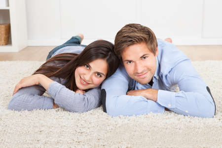 Portrait of happy couple lying on rug in living roomの写真素材