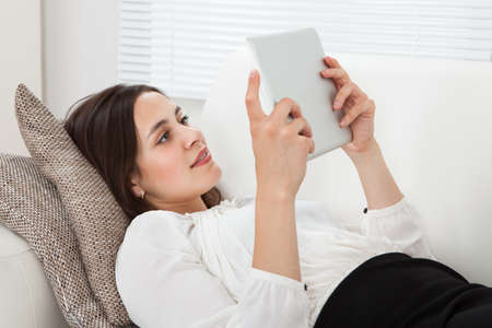 Full length side view of young businesswoman using digital tablet while lying on sofa at home