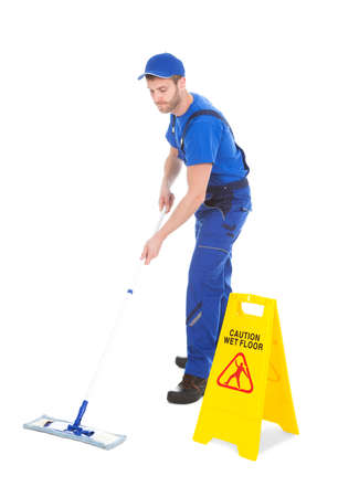 Full length of male servant mopping floor by Wet Floor Sign over white backgroundの写真素材