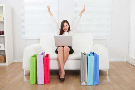 Full length portrait of excited businesswoman with laptop shopping online on sofa at homeの写真素材