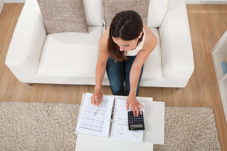 Portrait of confident young woman calculating home finances at table in houseの写真素材