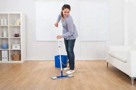 Full length of young woman cleaning hardwood floor of living room at home