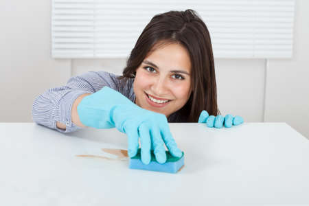 Close-up of woman's hand cleaning dirt on table with sponge at home