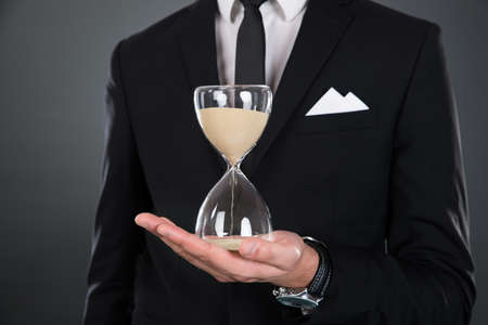 Midsection of businessman holding hourglass isolated against gray background