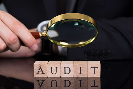 Midsection of young businessman examining Audit blocks through magnifying glass on deskの写真素材