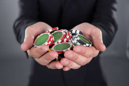 Midsection of businessman holding poker chips in cupped hands against gray backgroundの写真素材
