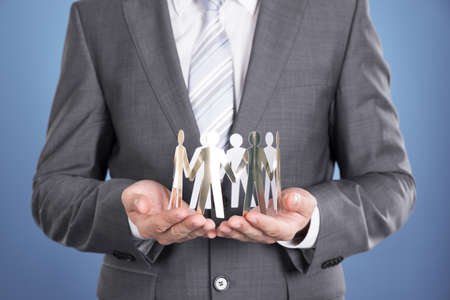 Businessman holding paper people. Over blue backgroundの写真素材