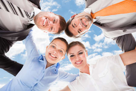 Directly below portrait of happy business people forming huddle against sky