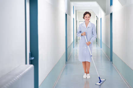 Full length portrait of happy cleaner mopping floor in hospitalの写真素材