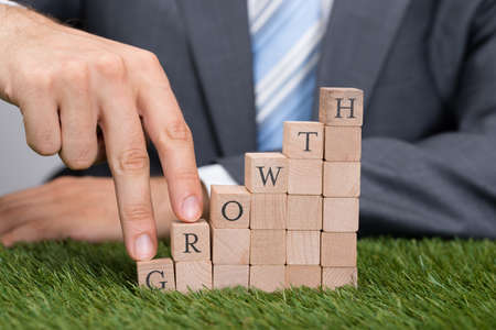 Midsection of businessman climbing growth blocks with fingers on grassの写真素材