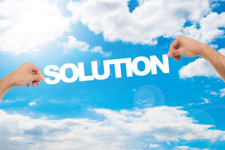 Cropped image of man's hands holding SOLUTION word against cloudy blue sky