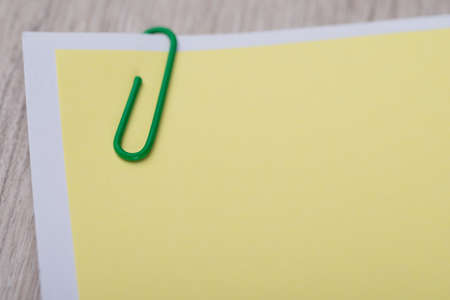 Blank yellow memo note with paperclip on tableの写真素材