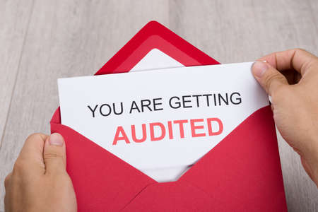 Cropped image of hand holding You Are Getting Audited card in envelope