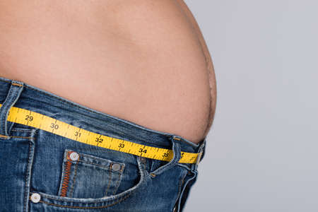 Side view midsection of fat man with measure tape around waist against gray backgroundの写真素材