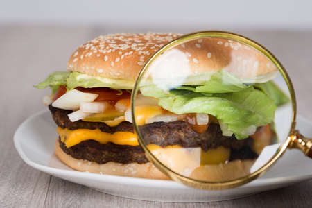 Closeup of magnifying glass examining burger in plateの写真素材