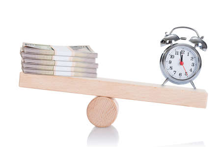 Alarmclock and dollar bundles balancing on seesaw isolated over white background