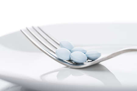 Closeup of tablets on fork in plate isolated over white backgroundの写真素材