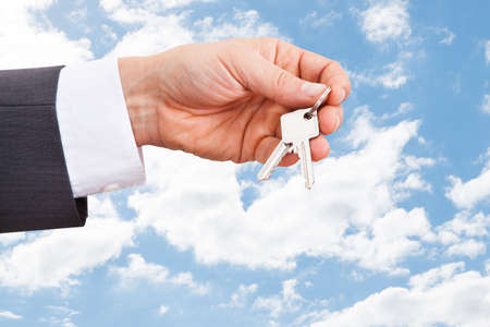Closeup of real estate agent's hand holding keys against cloudy skyの写真素材