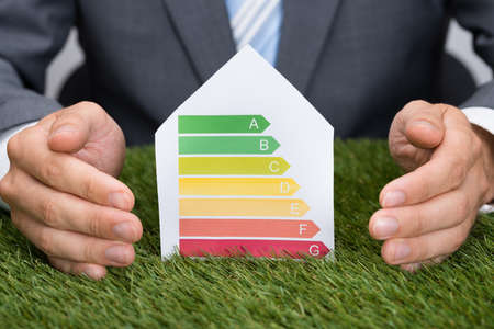 Midsection of businessman protecting house with energy consumption label on grassの写真素材
