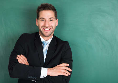 Portrait of happy young businessman standing arms crossed over green background