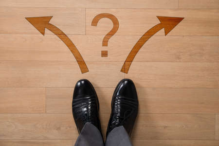 Low section of businessman standing in front of left or right arrows and question mark on floorの写真素材