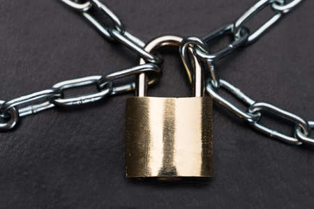 Closeup of metallic padlock and chains isolated over black backgroundの写真素材