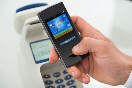 Closeup of businessman's hand paying through mobilephone in office