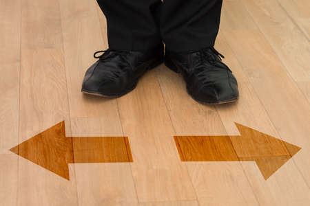 Low section of businessman standing in front of left or right arrows on floor